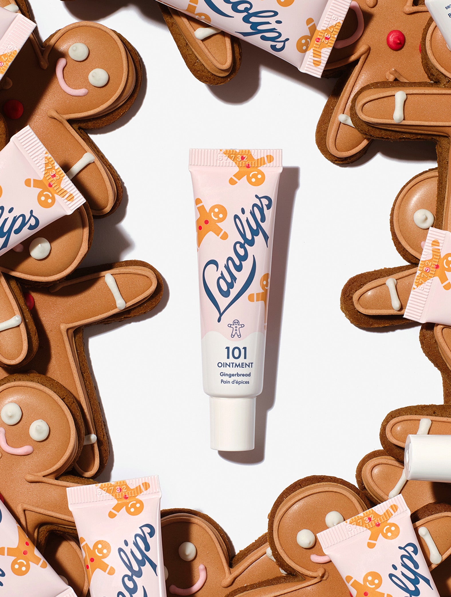 Tubes of Lanolips 101 Ointment Multi-Balm Gingerbread tube surrounded by gingerbread man-shaped cookies on a white background. Your lips have never tasted as sweet as this!