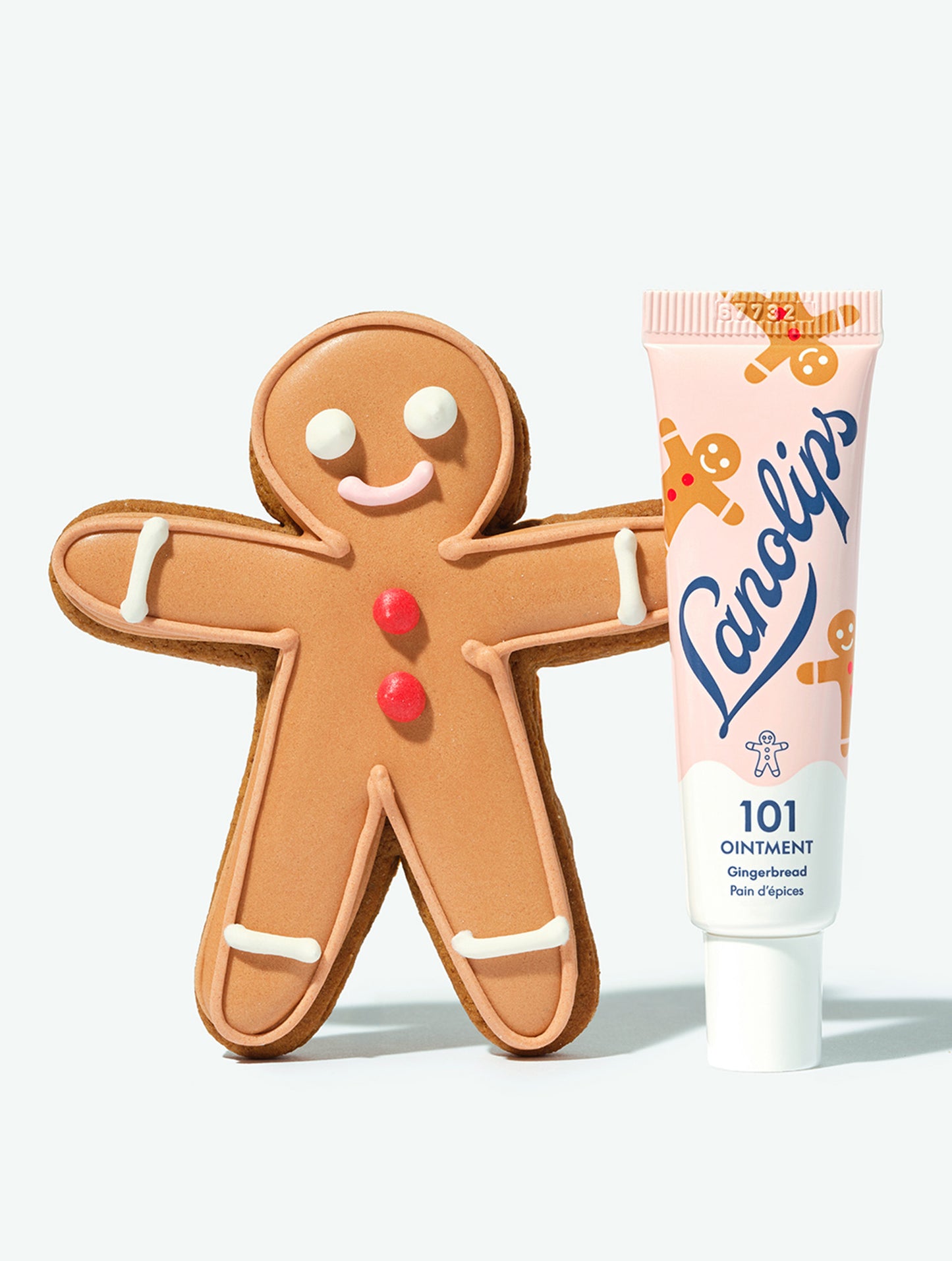 A tube of Lanolips 101 Ointment Multi-Balm Gingerbread lip balm leaning against a gingerbread man cookie. 
