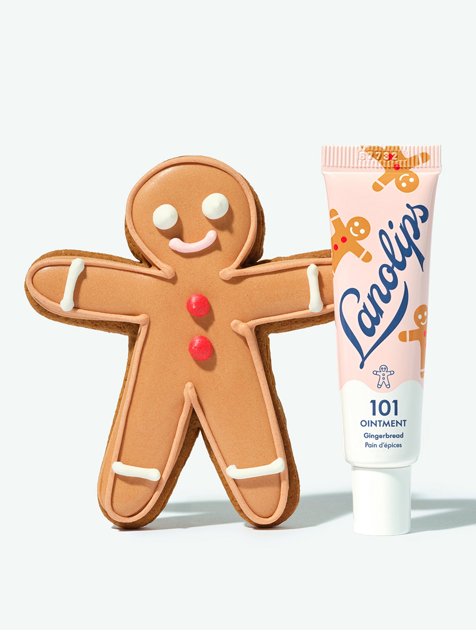 A tube of Lanolips 101 Ointment Multi-Balm Gingerbread lip balm leaning against a gingerbread man cookie. 
