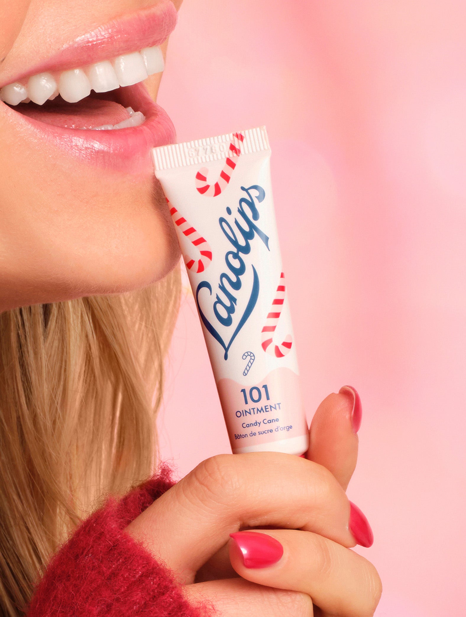 Model holding a Lanolips 101 Ointment Multi-Balm Candy Cane lip balm tube with a pink background.